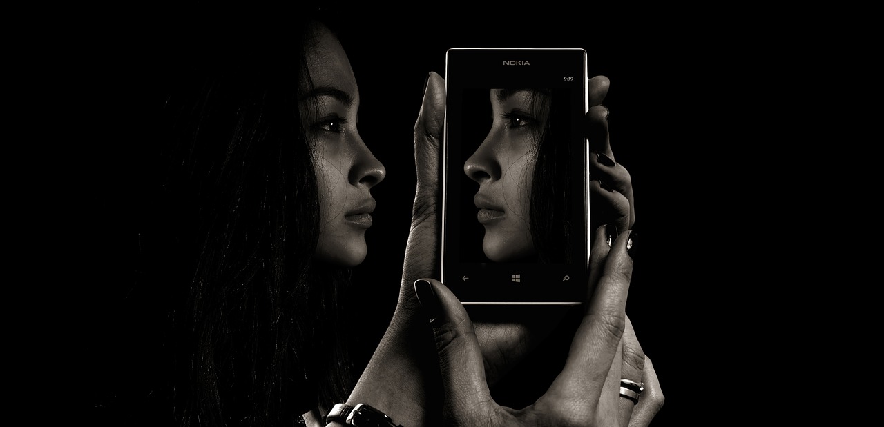 L'immagine mostra una ragazza che si specchia virtualmente in uno smartphone